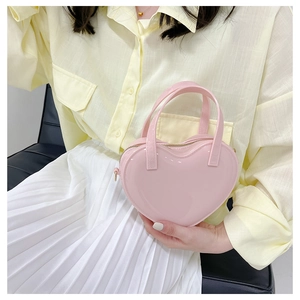 Pink heart-shaped jelly purse in glossy patent leather held by model for scale