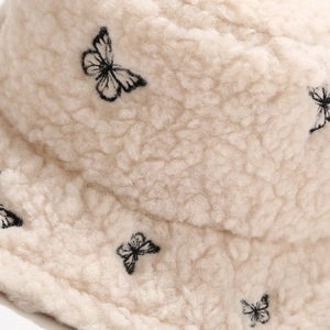 Macro detail of beige teddy fleece texture with black butterfly embroidery on bucket hat