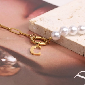 Detail of pearl and gold chain necklace with a polished letter C pendant on a buckle