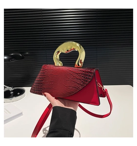 Detail of red crocodile texture handbag featuring a sculptural gold handle and strap
