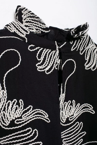 Close-up of black high-neck blouse with white embroidery and back button detail