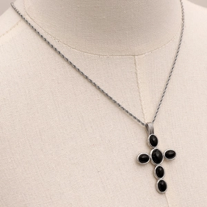 Detail of cross necklace with black natural stones on rope chain over beige fabric