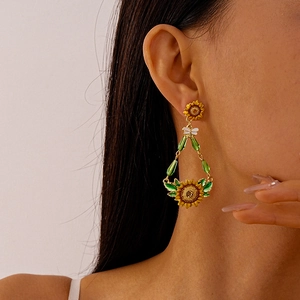 Close-up of dangling sunflower earrings with green crystal drops on a female model