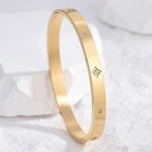 Polished gold bangle with star engraving and round crystals on a white pedestal