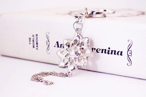 Close-up of a silver flower keychain with pearls and crystals on a white book surface