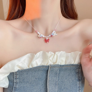 Detailed view of colorful butterfly and flower pendant necklace worn on model neck