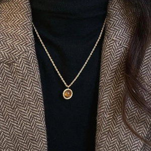Retro golden twisted chain necklace with round tiger eye pendant on a black sweater