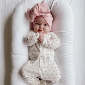 Close-up of a baby wearing a pink knit bow headband and white patterned romper