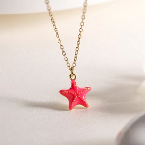 Vue macro du pendentif étoile de mer plaqué or avec émail rose foncé et billes dorées