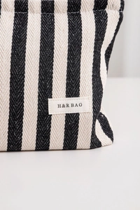 Detailed macro view of the striped canvas texture and H&R BAG woven label on the cosmetic pouch