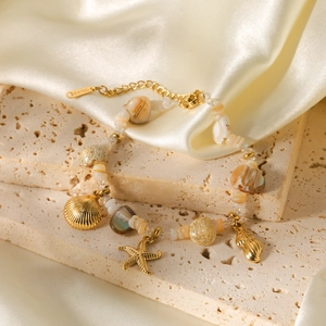 Gold stainless steel starfish and seashell beaded bracelet on a neutral stone background