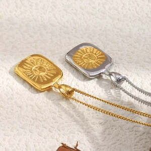 Détails de pendentifs soleil carrés en finitions or et argent sur surface texturée