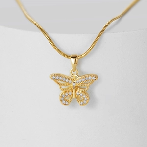 Gold butterfly pendant necklace with white cubic zirconia on a minimalist textured surface