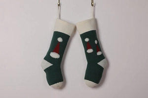 Detail of two green knitted Christmas stockings with red Santa hat pattern on white wall