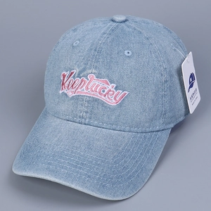 Detailed close-up of light blue denim baseball cap with Keep Lucky pink embroidery