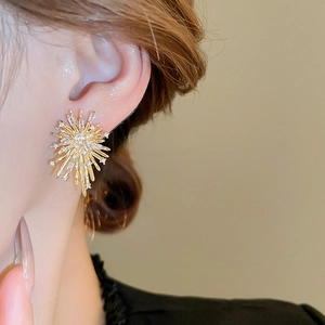 Close-up of golden starburst earrings with sparkling zircon stones worn by a model