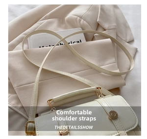 Detail of creamy white crossbody bag showing slim strap, stitching, and gold metal buckle