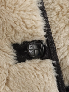 Dettaglio del bottone nero intrecciato sul cappotto in lana con finiture in pelle
