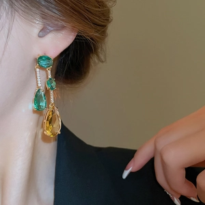 Détail de boucles d'oreilles à pompon avec zircons verts et jaunes sur base dorée