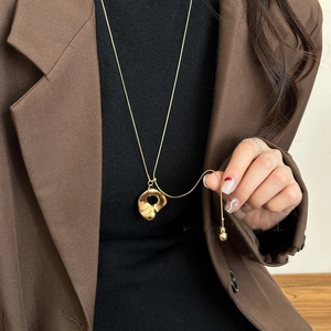 Close-up of golden irregular geometric hollow pendant necklace styled with a brown blazer