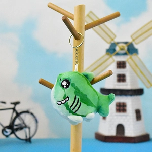 Cute green plush shark keychain with watermelon pattern hanging on a wooden stand.