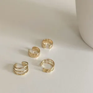 Detailed view of four minimalist golden ear cuffs set on a clean beige background
