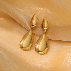Macro detail of gold teardrop earrings on luxury silk texture background