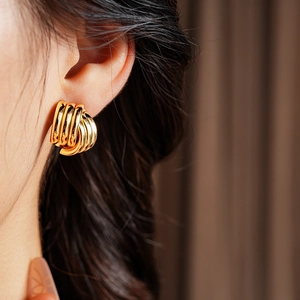 Close-up of a layered golden geometric earring worn by a model with a glossy metal finish
