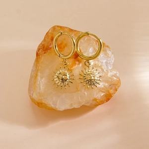 Dettaglio di orecchini a cerchio con sole 14K placcati oro appesi a una pietra naturale