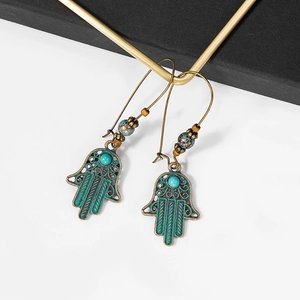 Detailed close-up of bronze Hamsa Hand earrings featuring turquoise beads and ornate carving