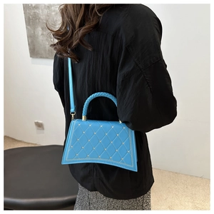 Blue trapezoid crossbody bag with diamond quilting and woven handle shown on model