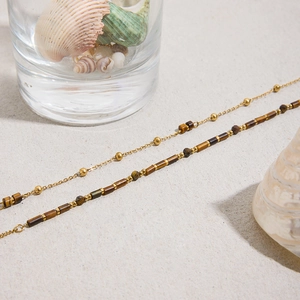 Close-up of layered tiger eye stone beads and gold plated chain necklaces on sand