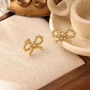 Detailed shot of gold-plated titanium steel bow earrings on a beige fabric display pad