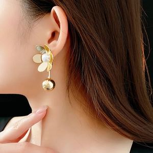 Gros plan de boucles d'oreilles fleur dorées avec perles et boules d'or sur un modèle
