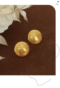 Macro detail of gold round earrings with water ripple texture on vintage brown felt