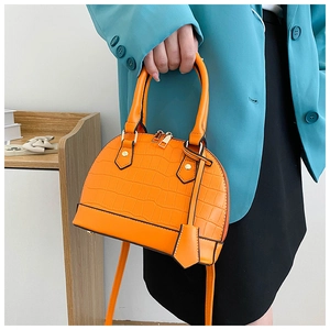 Detail of bright orange shell handbag with crocodile embossing and golden metal hardware