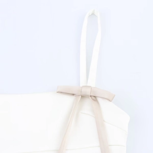 Close-up of white satin dress featuring beige bow decoration and delicate thin straps