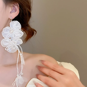 Detail of white fabric flower earrings with pearl tassels shown on a model