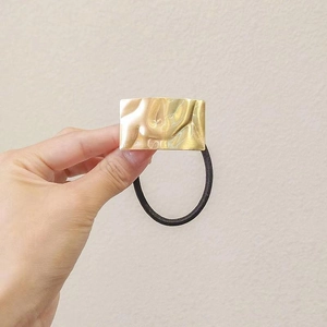 Dettaglio macro di elastico per capelli dorato con trama a lava e fascia elastica nera