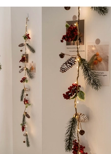Close-up of LED Christmas garland with pine cones, red berries and warm glowing copper lights