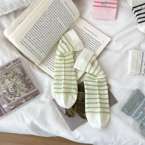 Detail showing green striped cotton socks with tiny embroidery on white bedding