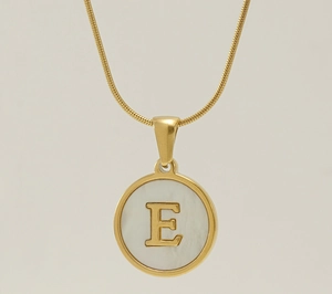 Close-up of golden snake chain necklace with round white shell pendant and letter E