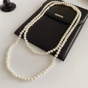 Long white pearl necklace elegantly draped over a black leather envelope bag detail