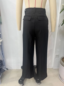 Detail of loose black wide-leg trousers featuring back flap pockets and textured woven fabric