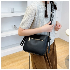 Detail of black crossbody bucket bag with front gold zipper and patterned woven strap