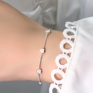 Detailed view of silver box chain bracelet with heart pendants on a woman's wrist