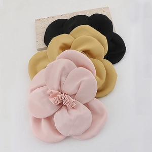 Three handmade fabric camellia flower brooches in pink, gold, and black on a stone base