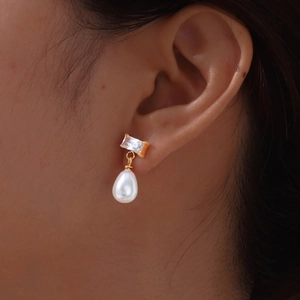 Detail of female model wearing gold pearl earrings with rectangle zircon and drop pearl
