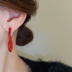 Side view of a vibrant red flame gourd shaped earring worn against black fabric