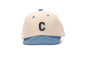 Detailed close-up of beige cotton baby cap featuring blue visor and embroidered letter C
